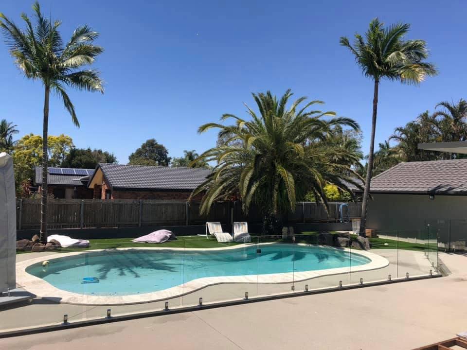 Frameless glass fence with silver spigots around a freeform pool